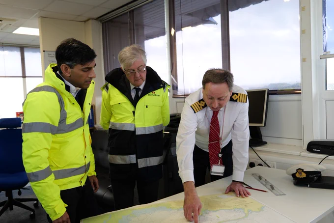 First Minister, Mark Drakeford and Prime Minister Rishi Sunak, meet with a captain in the port who explains to them in detail how the port operates. They stand looking at a nautical map of the area.