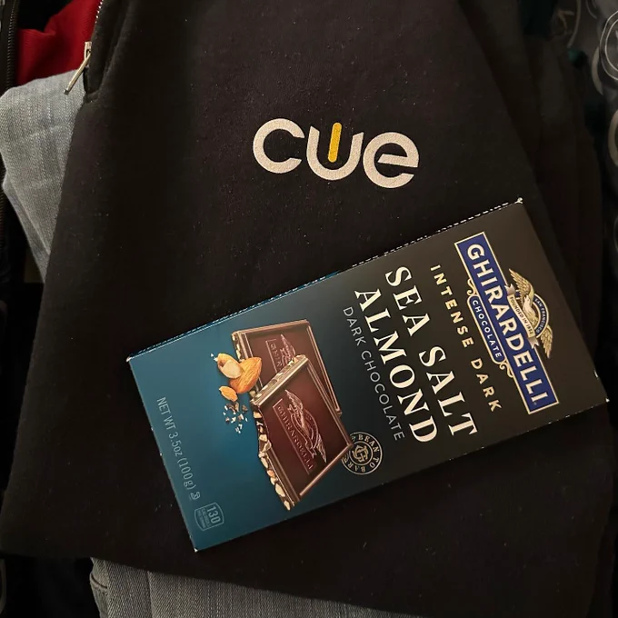 Ghirardelli intense dark chocolate sea salt almond chocolate bar on top of black sweatshirt with CUE logo. 