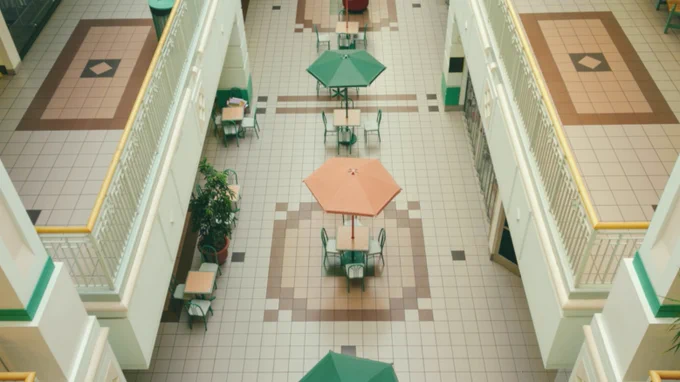 Two levels of an empty shopping mall which includes an eating area that has peach and teal umbrellas over the tables.