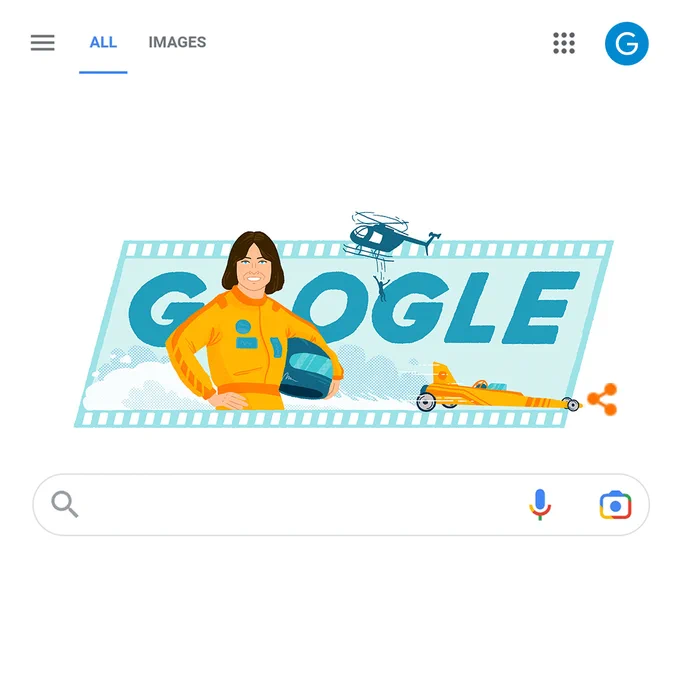 Google Search Page UI with the doodle in the middle containing a film strip in the background with ‘Google’ written on it and Kitty O’ Neil’s illustration in the front, with a race car at the bottom right and a helicopter with somebody jumping off it at the top, demonstrating her work as a stunt-woman. Above the doodle is the button tray containing the ‘All’ and ‘Images’ search options, and below it is the Google Search bar.