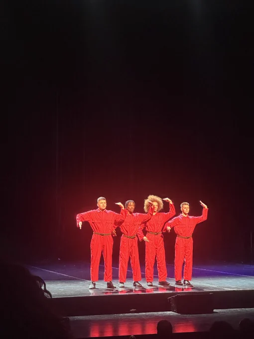 Billy Reid with his ‘cog in a wheel’ dance group Warren Murray, Ben Randall and Kameel Myrie performing live on stage in bright red boiler suits