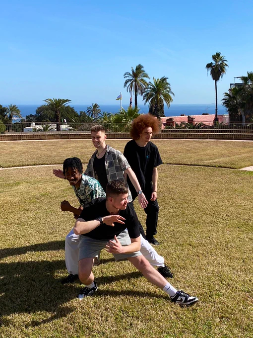 Billy Read, Warren Murray, Ben Randall and Kameel Myrie in a dance formation on the lawn at the British Ambassador’s Residence in Algiers. Palm trees, sea and blue sky in the background