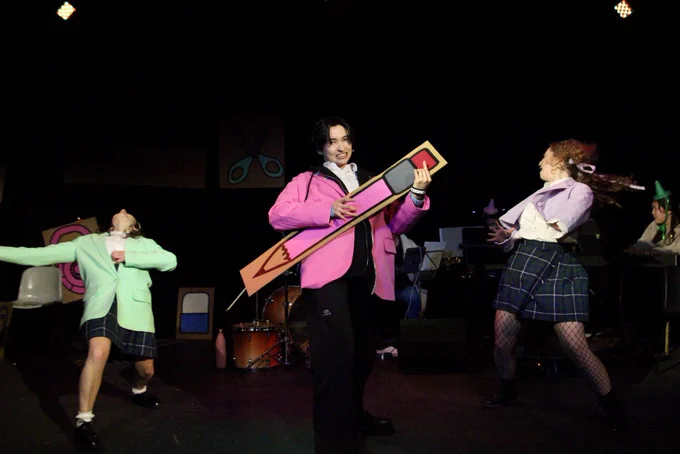 The cast rock out and dance around the stage. Ashley in pink is holding a giant pink pencil.