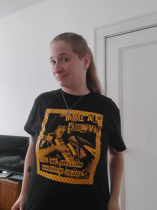 Me looking at the camera. I am wearing a black t-shirt screen printed with a vintage "Weird Al" Yankovic logo from his first album, Weird Al playing on the accordion, and the phrase "I'll Be Mellow When I'm Dead."