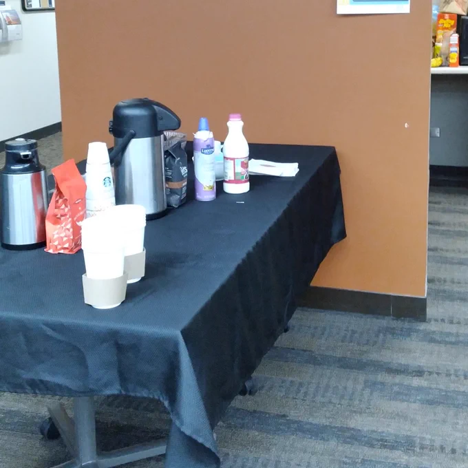 Photo of a table with a black tablecloth, coffee carafes, and coffee creamer.