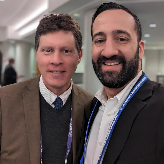 Two men in blazers stand for a selfie in a hotel conference lobby. 