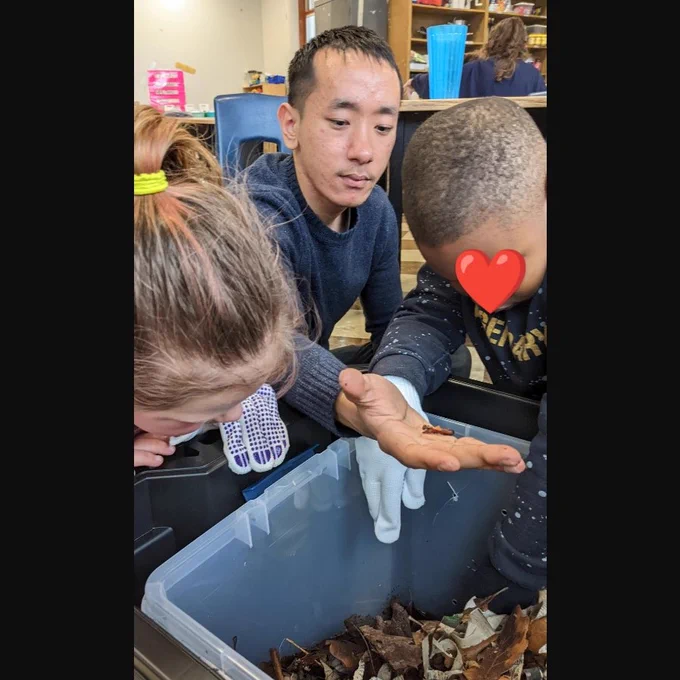Two children and a college student looking through compost bin for worms.