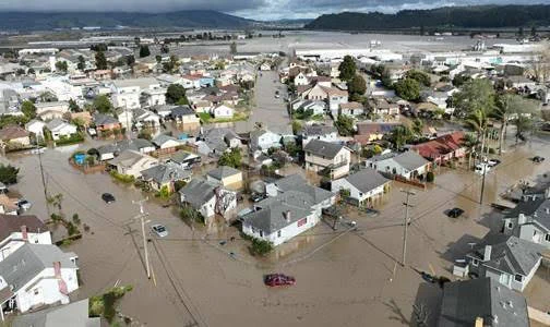 An aerial view of a residential neighborhood in Pajaro, California, showing homes surrounded by flooded streets. 