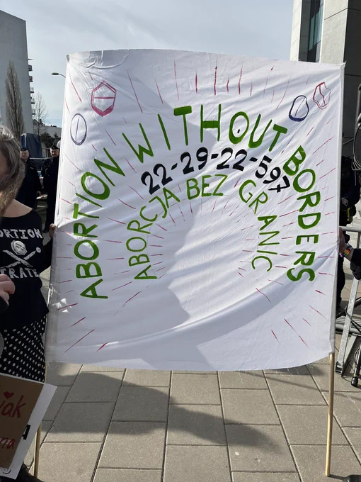 A hand-painted sign with the words “Abortion Without Borders, 22-29-22-597, Aborcja Bez Granic”. The phone number is the Abortion Without Borders helpline.