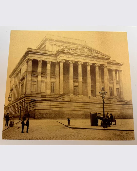 
Harris Museum exterior at the front, dated 1894. There are people standing on the flag market in front of it, including near the lamppost or people sitting on a bench. 
