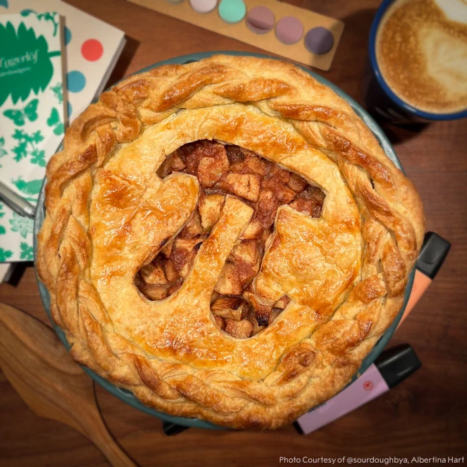 A golden brown apple pie with the 'pi' symbol cut into it. 