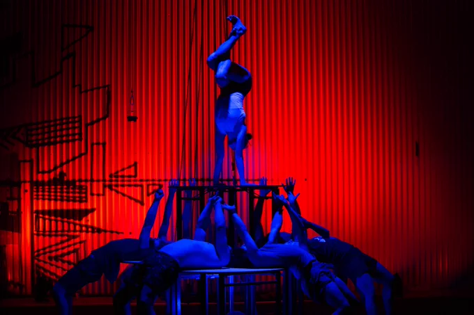 Out of Chaos, credit Carnival Cinema. An acrobat does a handstand supported by other acrobats against a dramatic red background