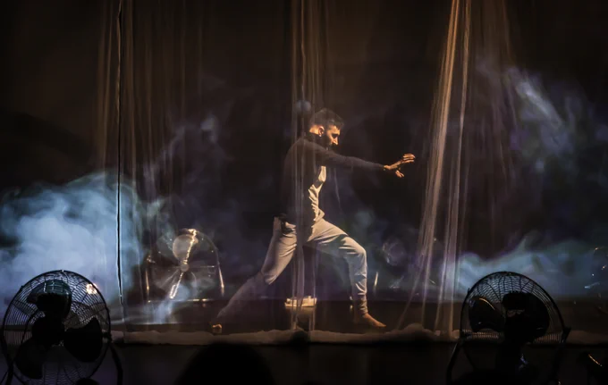 Little Murmur, credit Pamela Raith Photography. A man stands on stage with hand outstretched, with mist and projections