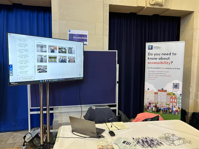 Large tv in background showing an Access Guide to Trent Building. Banner stand advertising AccessAble at the University with the title ‘do you need to know about accessibility’ in the foreground is a table l, on that table are AccessAble branded pens and key rings.