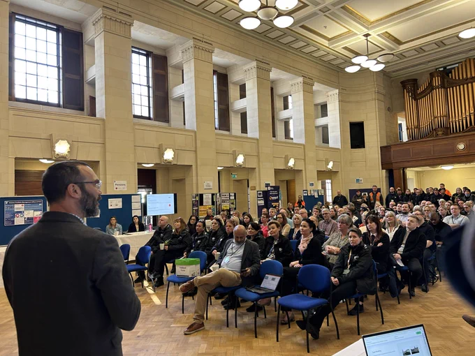 The great Hall at Trent Building full of people seated watching AccessAble’s Director David Livermore deliver a presentation on the AccessAble University of Mottingham project. The photo is taken over the shoulder of David with the audience in the background.