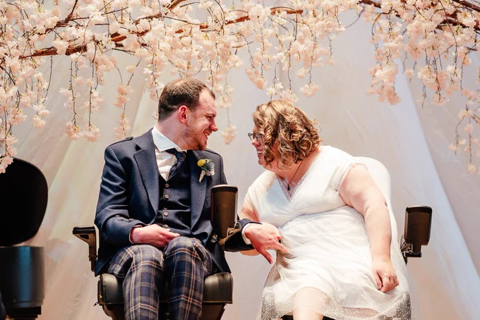 Zara and Alex getting married under a cherry blossom archway 