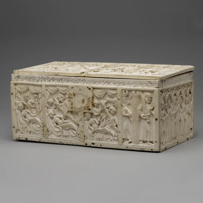The lid of a white rectangular ivory box, which has been separated into eight squares. Each one has a different scene of medieval courtly life. In one scene a couple embrace on a bed while a small dog sits beside them.