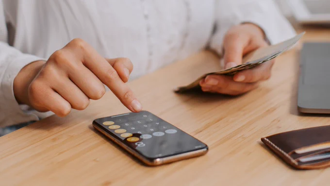 Hands typing on calculator and holding money