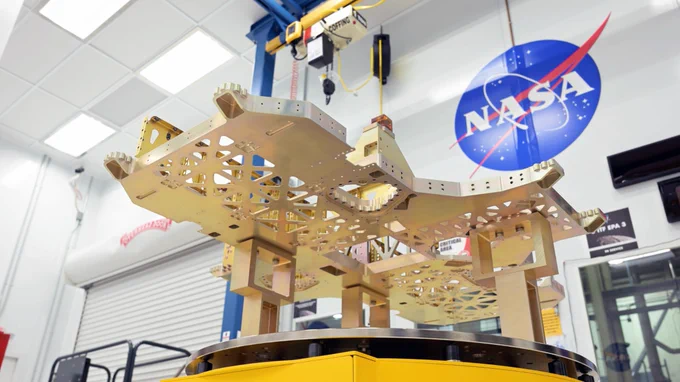 A view from beneath of the chassis, a base component for the VIPER Moon rover. Its a metallic shape with cutouts and a combination of sharp and curved edges. It is placed atop a pedastal in the VIPER clean room at NASA's Johnson Space Center in Houston. Credit: NASA