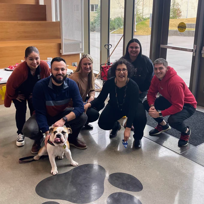 Group of people crouching to pose for a photo with the new live mascot puppy.