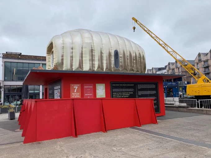 red and silver small building designed to replicate what a house on Mars may look like. Yellow crane beside it.