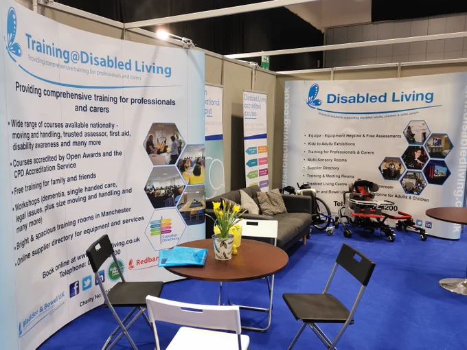 An image of the Disabled Living stand. There are signs up for training and tables, chairs, a sofa and equipment.