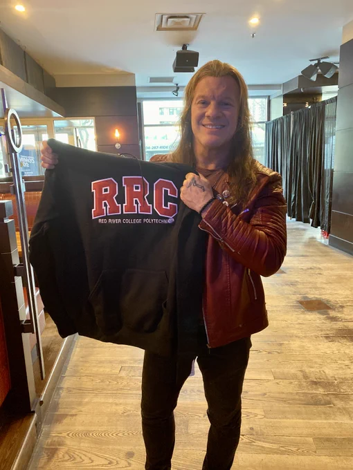 Distinguished Graduate and Creative Communications grad, Chris Jericho holding an RRC Polytechnic branded hoodie.
