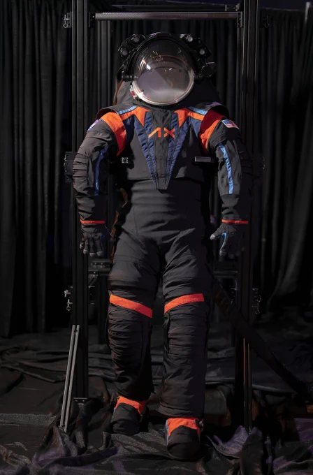 The Artemis III spacesuit prototype, the AxEMU, is on display with a black background. The prototype is primarily dark gray with orange stripes at the joints and has blue accents on the chest and arms. Credit: Axiom Space
