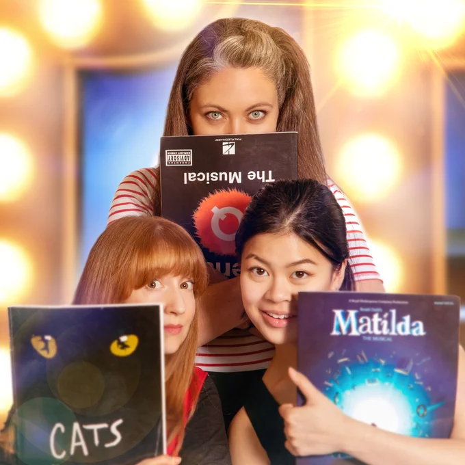 Three performs look into the camera, holding musical theatre song books in front of them. There are glitzy lights in the background.

