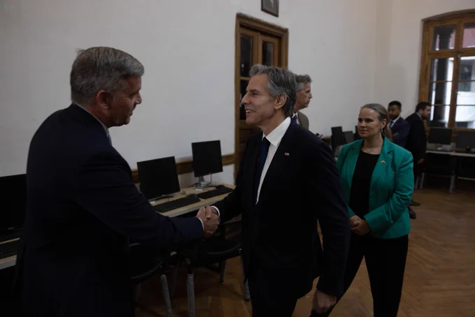 Secretary Blinken shakes hands with a man during a meeting with human rights leaders and advocates. Four people stand in the distance behind them.