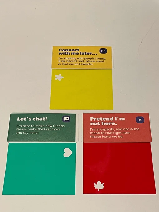 Image of color communication badges. The Yellow badge says "connect with me later" and has a flower hole punch, the green says "let's chat" and has a heart hole punch" and the red says "pretend I'm not here" and has a maple leaf hole punch.