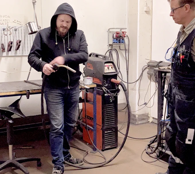 A man, with welding equipment, teaching another man.