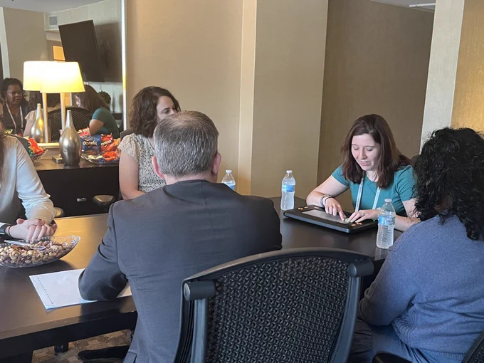 Five people sit around a table. One person is using the Monarch on the table in front of them.