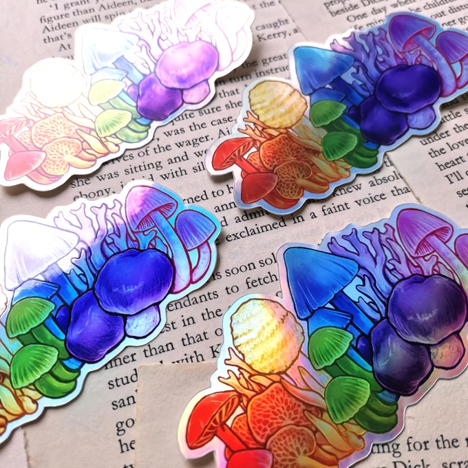 four of the rainbow mushrooms on a book page background, with light reflections showing some holo