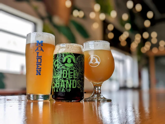 3 beers on a wooden table in Idle Hands branded glassware.