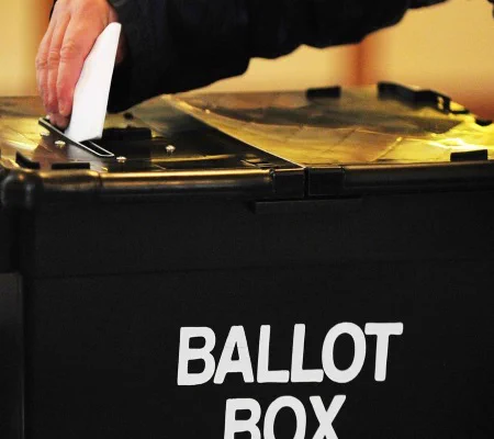 a ballot box with a hand placing a voting slip in