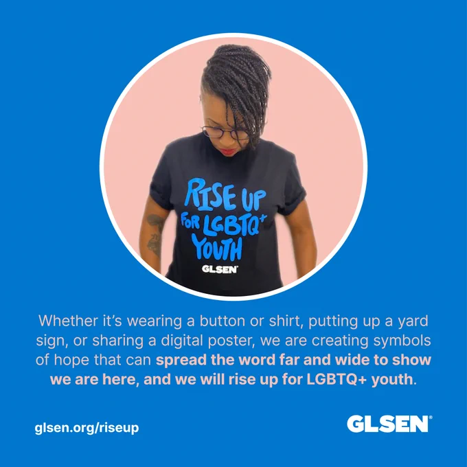  Image of Mel wearing a black shirt that says "Rise Up for LGBTQ  Youth" with the text "Whether it's wearing a button or shirt, or sharing a digital poster, we are creating symbols of hope that can spread the word far and wide to show we are here, and we will Rise Up for LGBTQ  Youth"