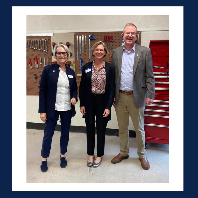Two women and a man are standing in front of a wall of tools. The first woman, Prof. Betsy Cantwell, is wearing navy blue dress pants and matching jacket. She has on a white shirt. The second woman, Prof. Liesl Folks, is wearing black dress pants and a matching sweater. She has on a red printed blouse. The man, Dean David W. Hahn, is wearing khaki slacks, a grey suit jacket and blue shirt. They are all smiling because the center has finally opened. 