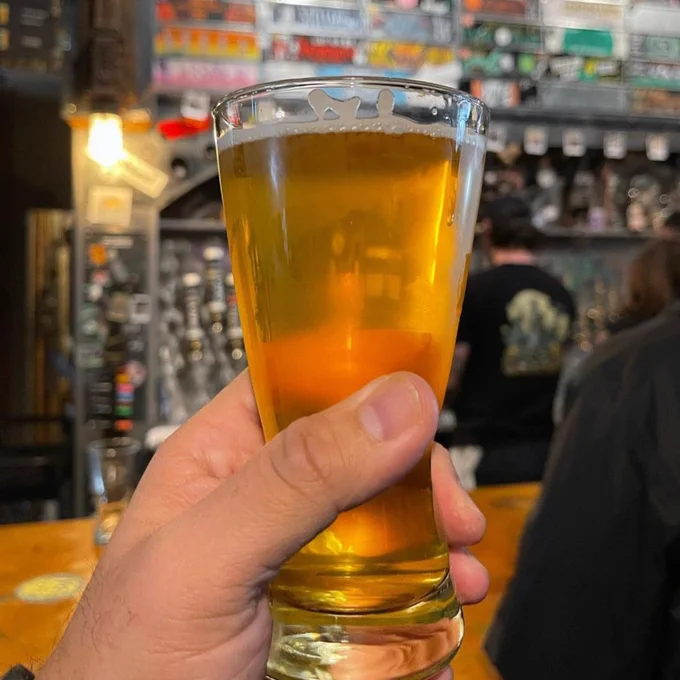 a glass of beer held up in front of a brewery bar