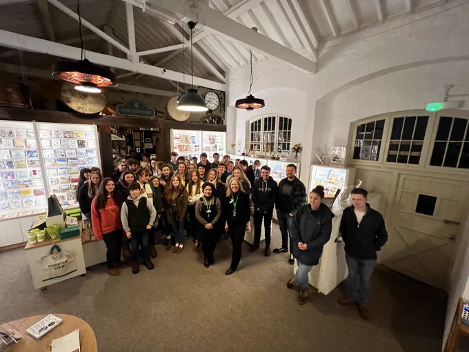 A group of about 40 people posting for a photograph in an old building with a wooden roof and modern shop floor.