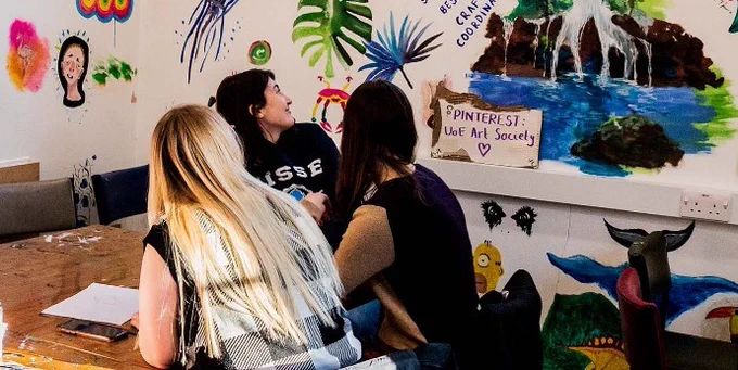 3 students looking at hand-painted art on the walls