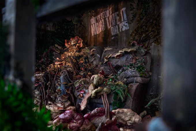 Another angle of the Cordyceps infected person on a sofa, the photo clearly showing the sofa is well-worn and covered in spores and fungi too.  Text on the wall behind them reads "You've Seen It, Now Live It on PS5".  They were located in BOXPARK Shoreditch in London. 