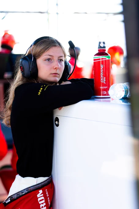 Doriane Pin leaning on a wall, which has on it a red water bottle with her name upon it in white font