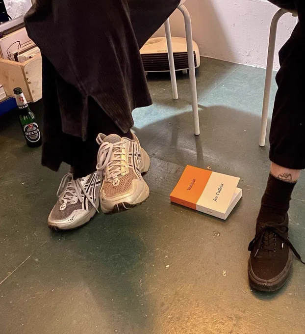 A picture of the speakers’ shoes, a pair of white trainers and blank plimsoles with the orange and white book on the floor between them