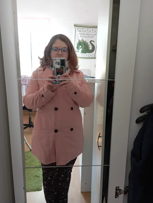 Person in rosa Trenchcoat steht vor einem Spiegel 