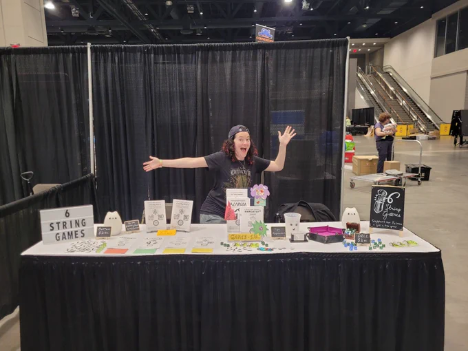 Anna striking an excited pose in front of a table set up for selling games