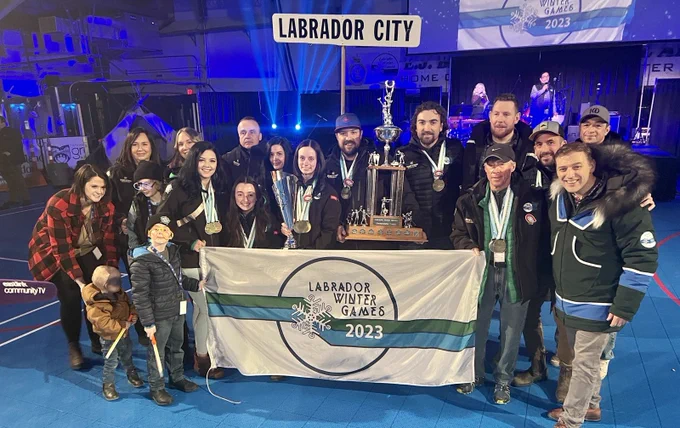 Group of Labrador City team members stand with trophy and Labrador Winter Games Flag