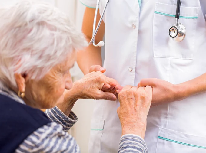 A doctor holds hands of an older woman. 
