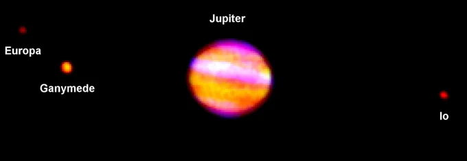 Jupiter appears as a pixelated blob of pink and orange against a black background. Its moons Ganymede, Europa, and Io are also in the image as orange and red dots, Ganymede and Europa on Jupiter's left, and Io on the right. 