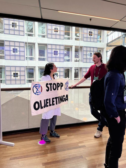 A scientist in a lab coat holding a banner reading "Stopp Oljeletinga" (Stop Oil Exploration) talks to a participant at the NTNU Energy Transition Conference